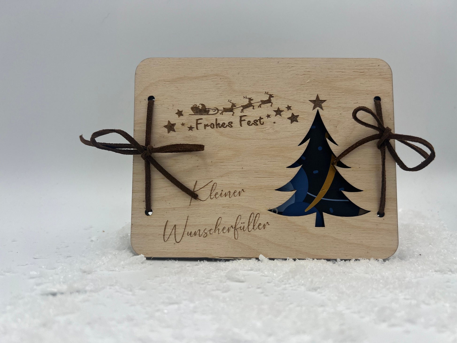 Holz-Geschenkkarte mit Weihnachtsbaum-Motiv, Frohes Fest-Gravur und Platz für Geldgeschenke, verziert mit Bändern.